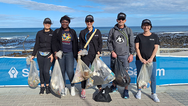 A picture of an Inspired Testing team with bags of litter after volunteering to clean up the Sea Point beach in Cape Town during a marathon.